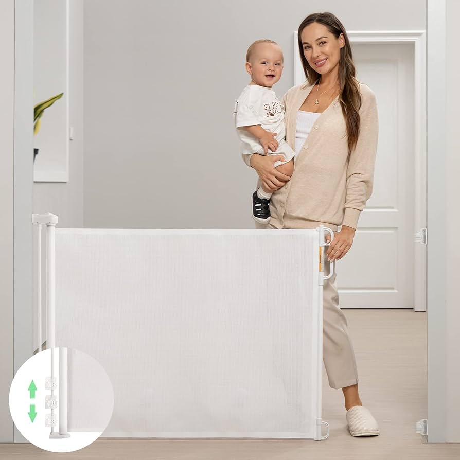 Retractable Momcozy baby gate extended across a stair entry with gray mesh and wall-mounted housing